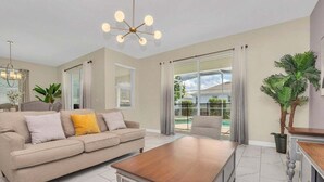Un salón amplio con un sofá color beige, una mesa de centro de madera y un ventanal con cortinas.