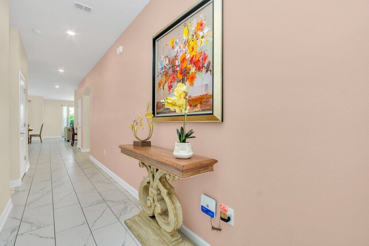 Un couloir doté d’un sol en marbre, d’une console en bois sur laquelle sont posés un vase et une sculpture, et d’un tableau encadré accroché au mur.