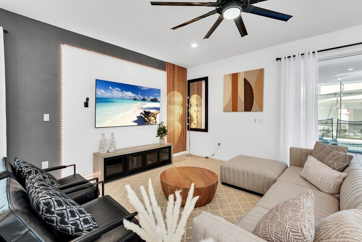 Una sala de estar moderna con un televisor de pantalla plana grande, un ventilador de techo y un ventanal con cortinas.