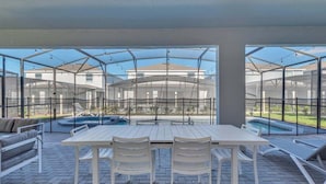 An outdoor patio with a white table and chairs, a pool, and a view of a residential area. - 3624ll · Brand New Luxury 8BR Villa in Windsor Island (Davenport)