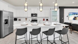 A modern kitchen with white cabinets, a stainless steel refrigerator, a central island with bar stools, and pendant lighting. - 3624ll · Brand New Luxury 8BR Villa in Windsor Island (Davenport)