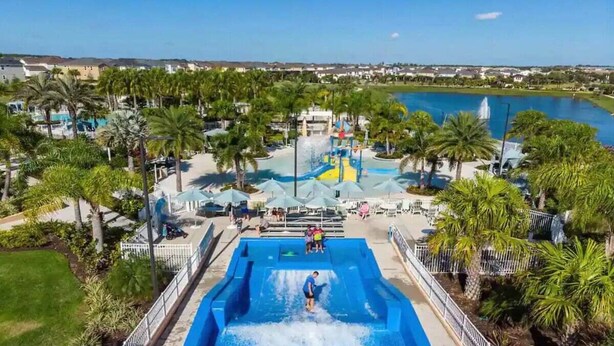 A water park with a large pool, palm trees, and a view of a lake. - 8939ad · Amazing Solara 7br/ Pool /spa /free Waterpark (Kissimmee)