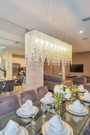 Zona pranzo con tavolo in vetro apparecchiata per sei persone, un lampadario e un design d'interni moderno.