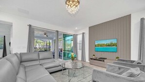 A modern living room with a sectional sofa, a glass coffee table, and a flat-screen TV mounted on the wall. - 8939ad · Amazing Solara 7br/ Pool /spa /free Waterpark (Kissimmee)