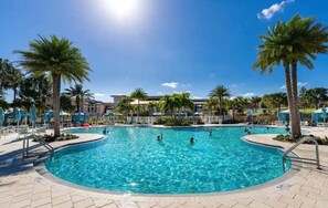 Une piscine bordée de palmiers, avec des chaises longues et un ciel dégagé.
