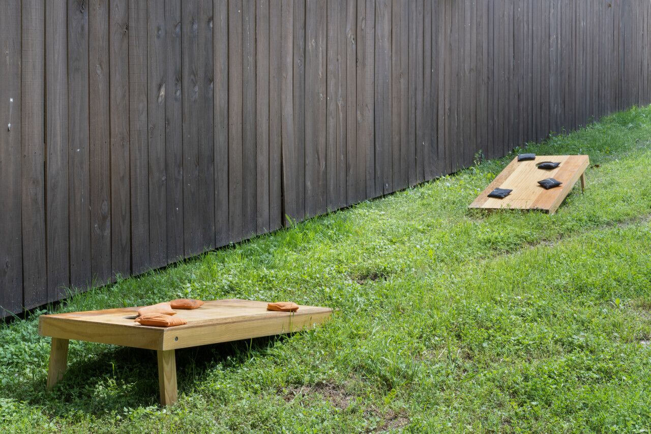 A wooden table with cushions on a grassy area next to a wooden fence.