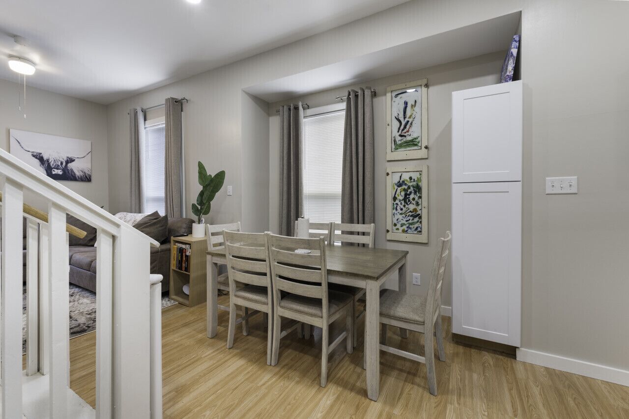 Un coin repas avec une table et des chaises en bois, un escalier menant à une autre pièce et un meuble blanc adossé au mur.