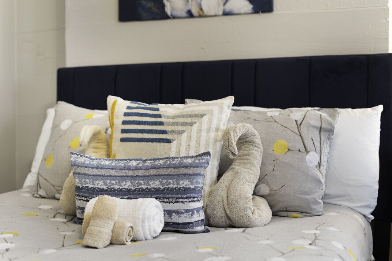 A neatly made bed with a dark headboard, multiple pillows, and a decorative pillow with a branch pattern.