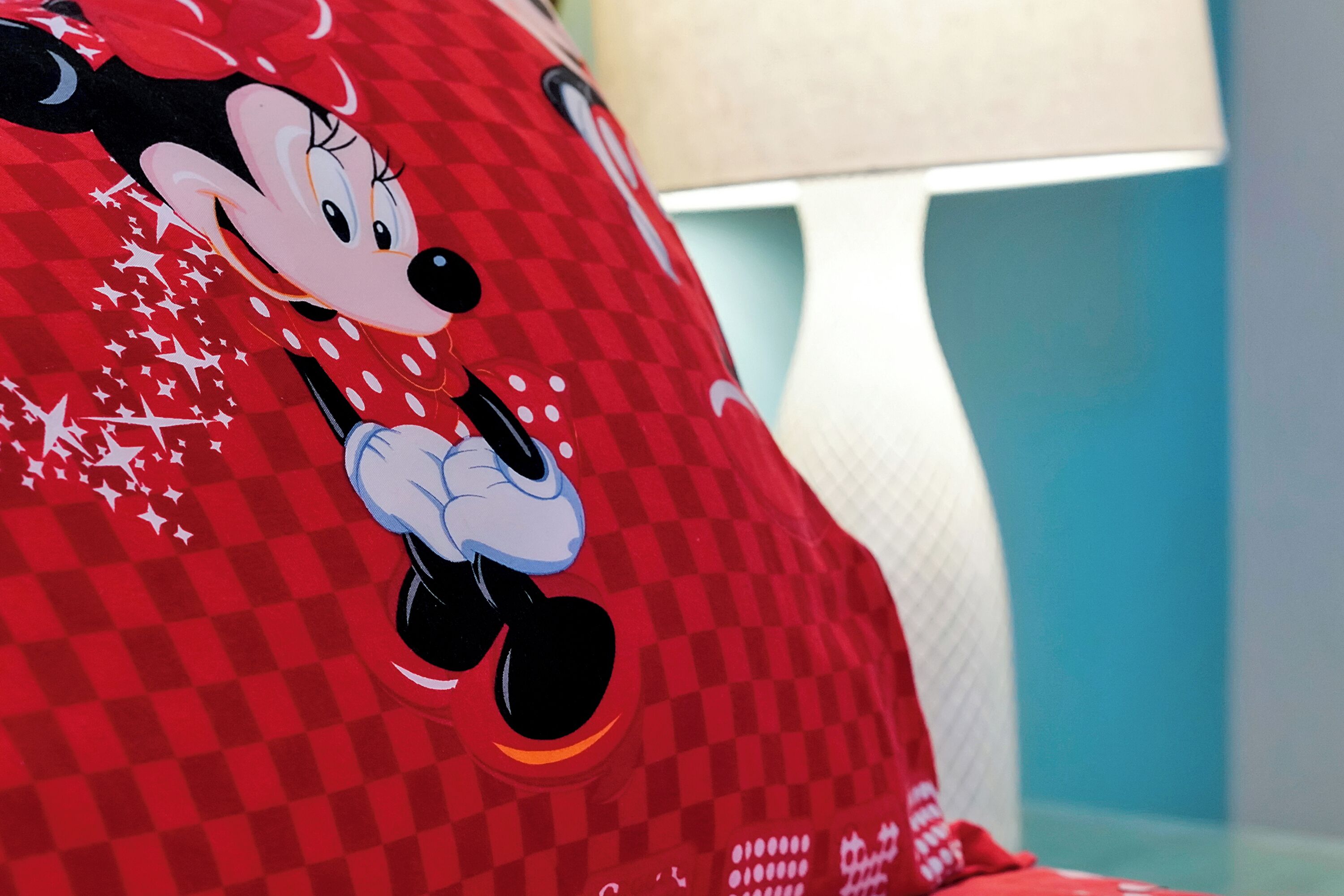 A Mickey Mouse pillow on a bed with a checkered pattern.