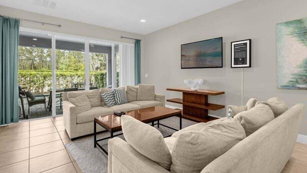 A spacious living room with a beige sofa set, a coffee table, and a wooden side table. There is a large window with a view of greenery outside. - 541-7-ld-dream Home - Private Pool&spa (Kissimmee)