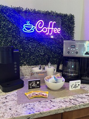 A coffee station with a neon sign, a coffee maker, a sign reading "Plus Vacation Homes," and a bowl of coffee packets. - 541-7-ld-dream Home - Private Pool&spa (Kissimmee)