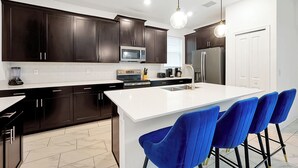 A modern kitchen with dark cabinets, a white island, and blue bar stools. - 1085 Leader ST, Davenport,5 BED (Davenport)