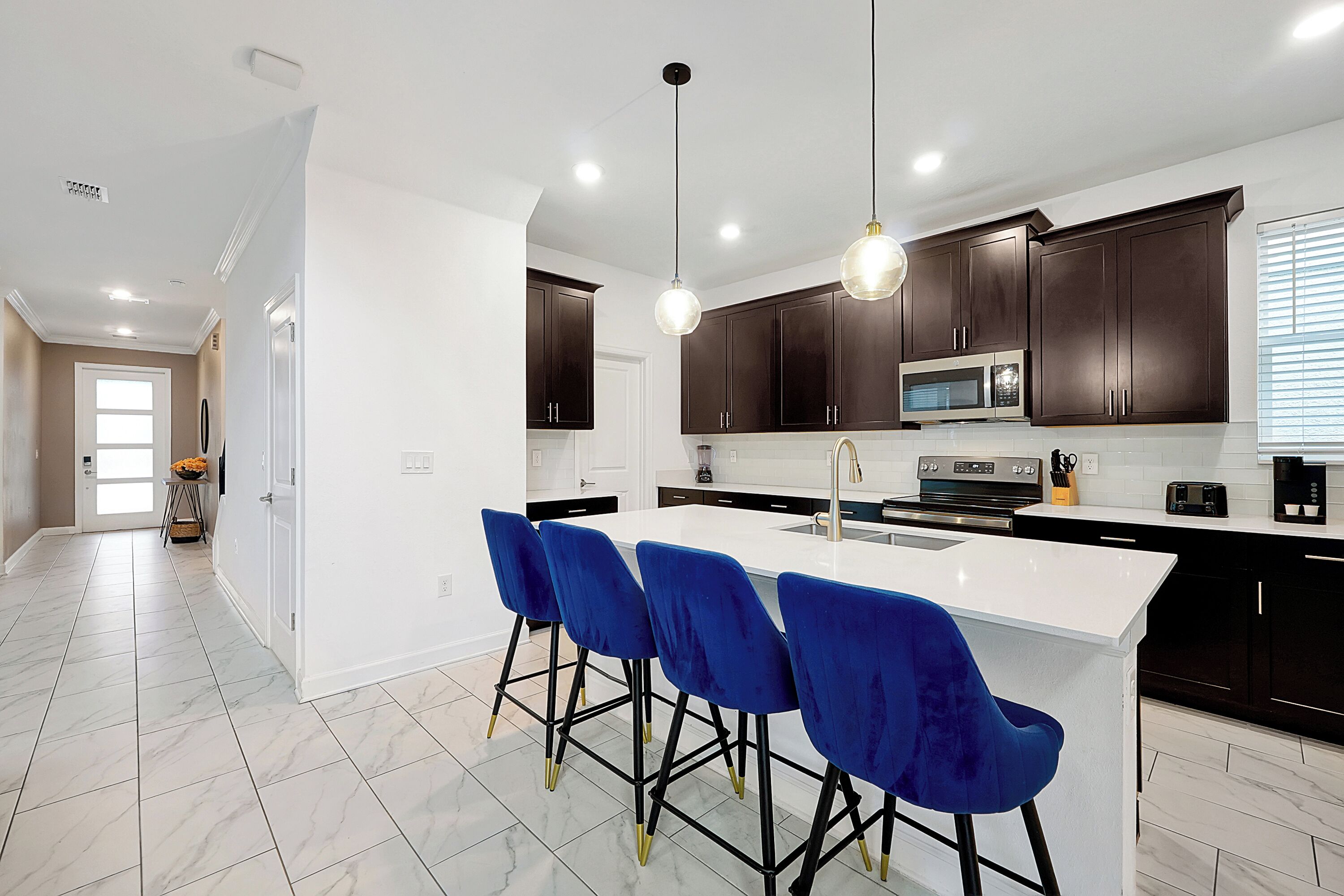 A modern kitchen with a white island, dark wooden cabinets, and blue bar stools.