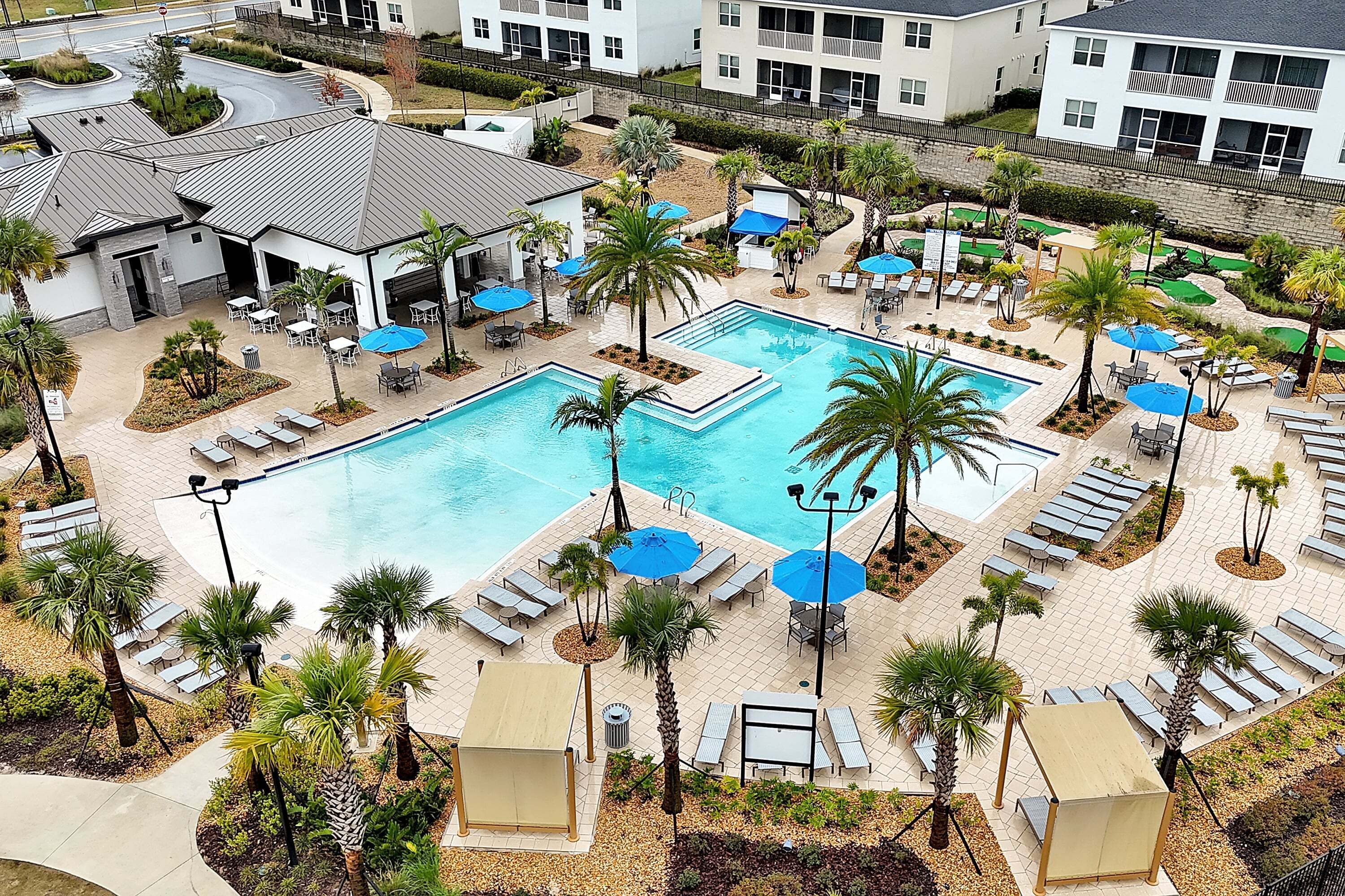 Un resort con piscina centrale, lettini prendisole e palme.