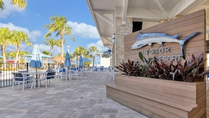 Der Eingang eines Resorts mit einem hölzernen Schild, Sitzgelegenheiten im Freien und Palmen.