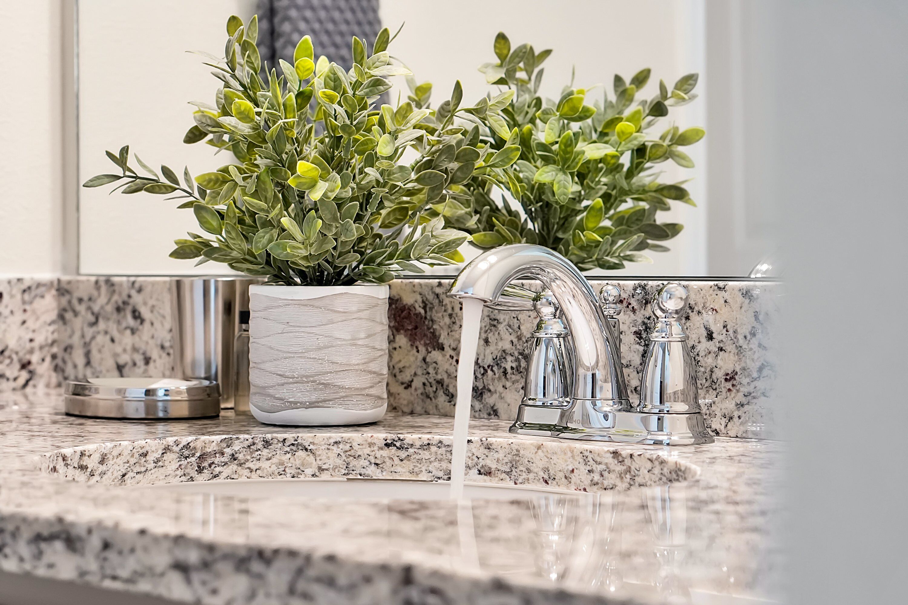 A bathroom with a granite countertop, a sink with a modern faucet, and two potted plants.