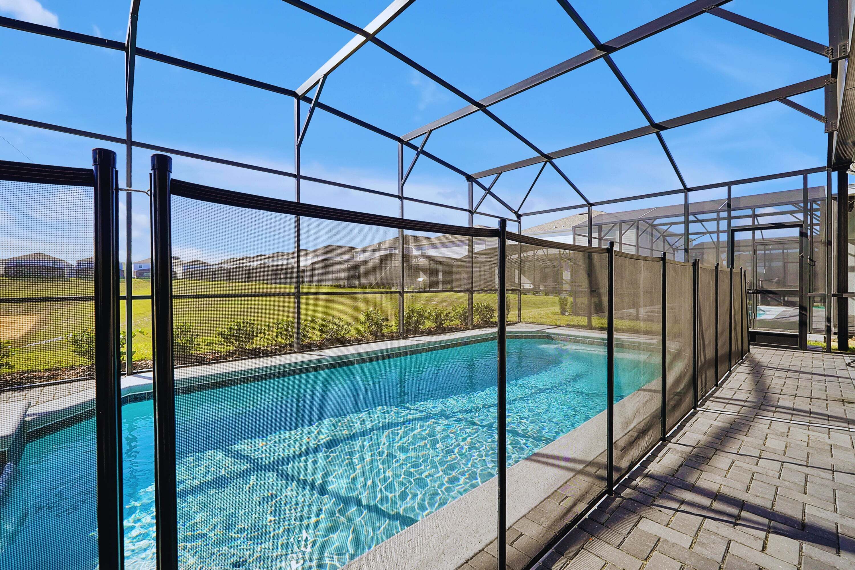 Una piscina con agua cristalina azul, rodeada por una zona cubierta con estructura metálica y vistas a un paisaje verde.