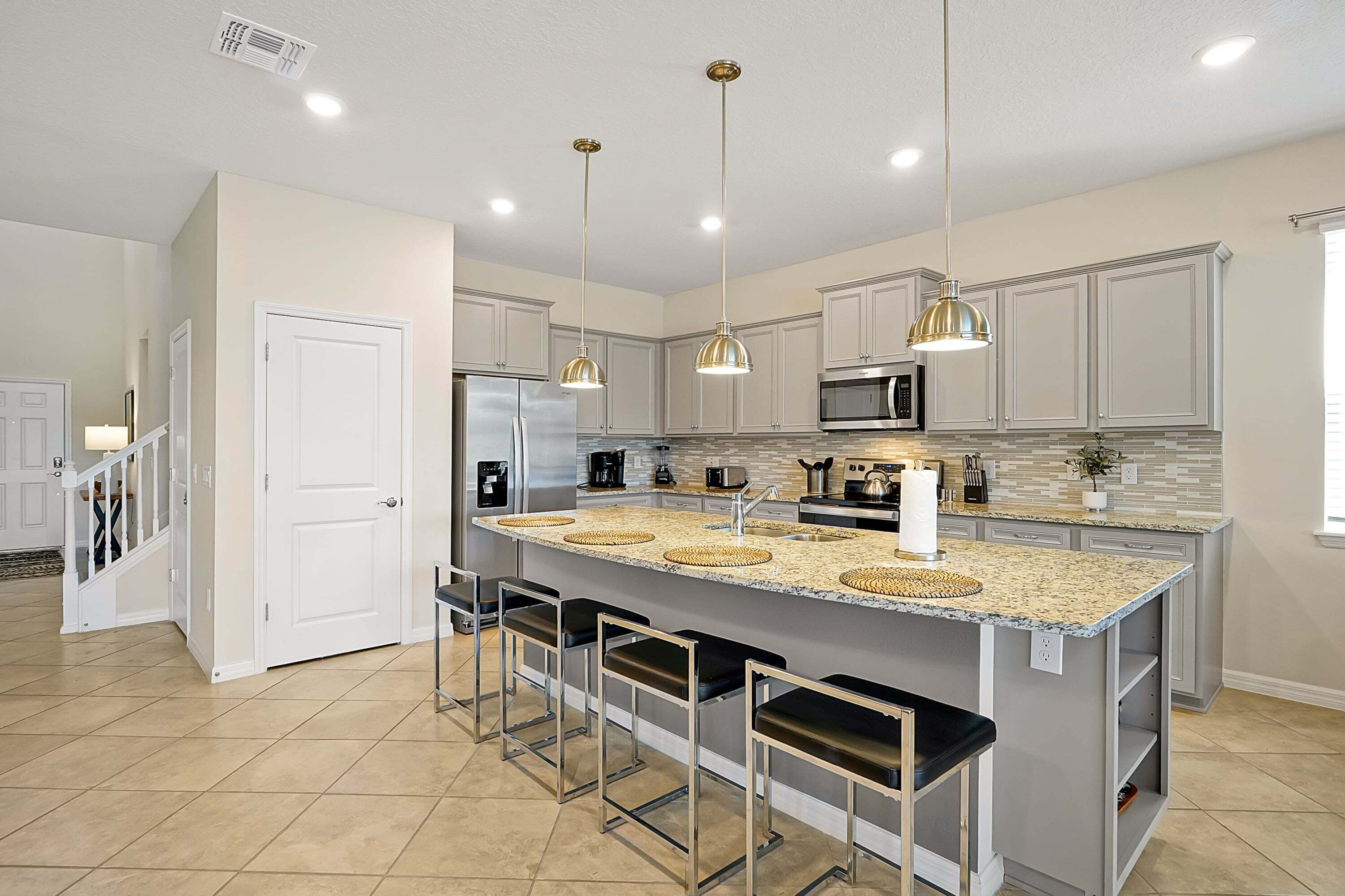 A modern kitchen with a large island, bar stools, stainless steel appliances, and pendant lighting.