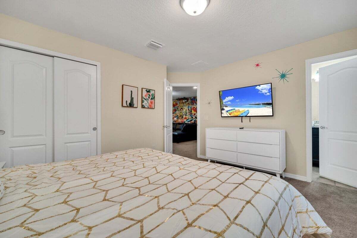 Een slaapkamer met een bed, televisie, dressoir en inloopkast.