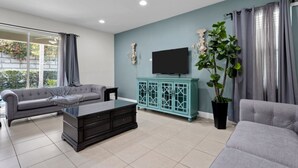 Ein modernes Wohnzimmer mit einem grauen Sofa, einem schwarzen Couchtisch, einem türkisfarbenen Schrank und einer großen Topfpflanze.