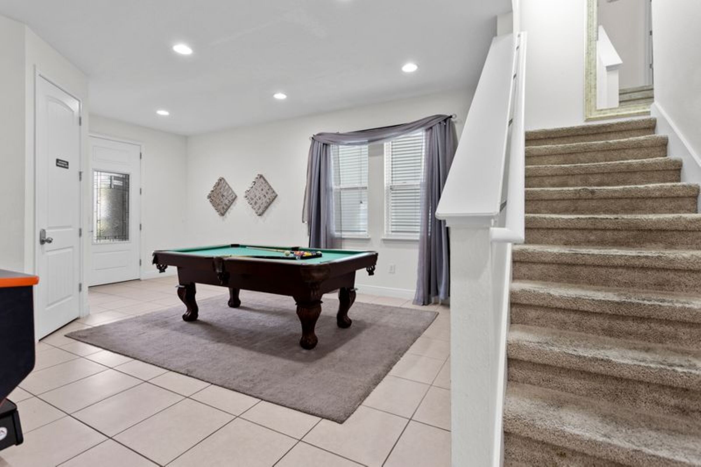 A room with a pool table, a staircase, and a door leading to another room.