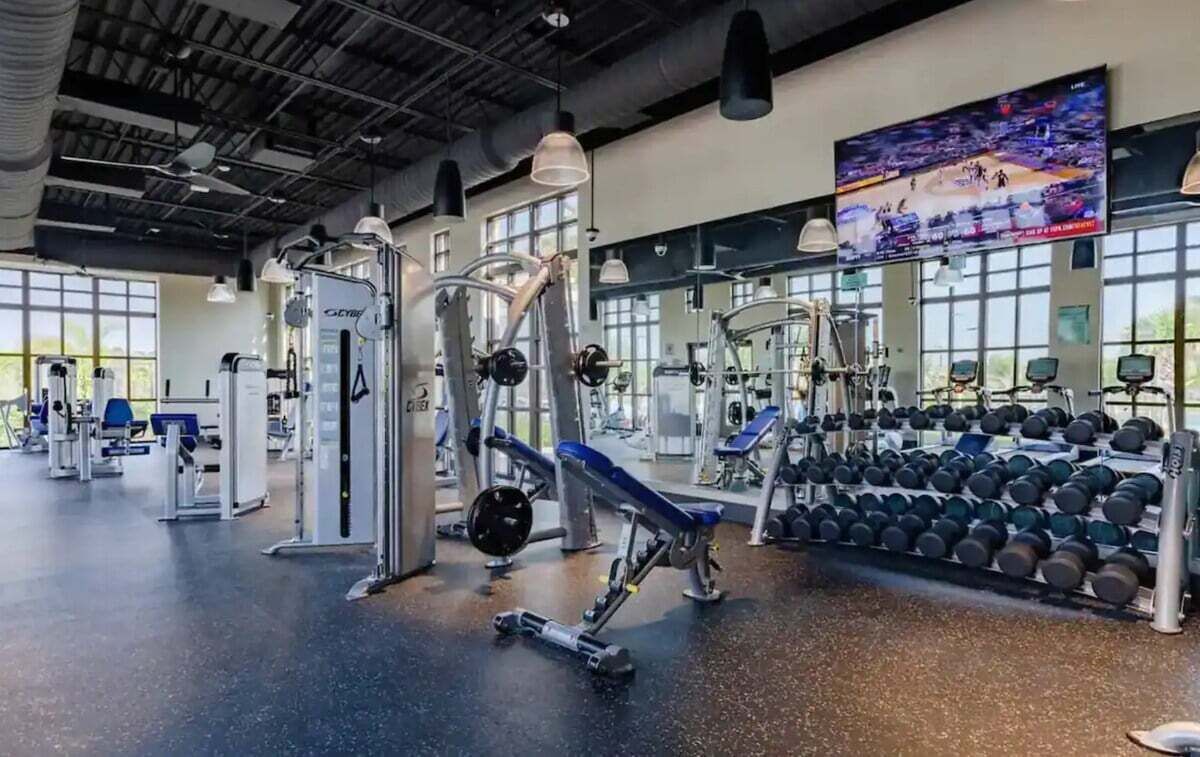 Un gimnasio con diverso equipo de ejercicio, una pantalla de televisión y un ventanal grande.
