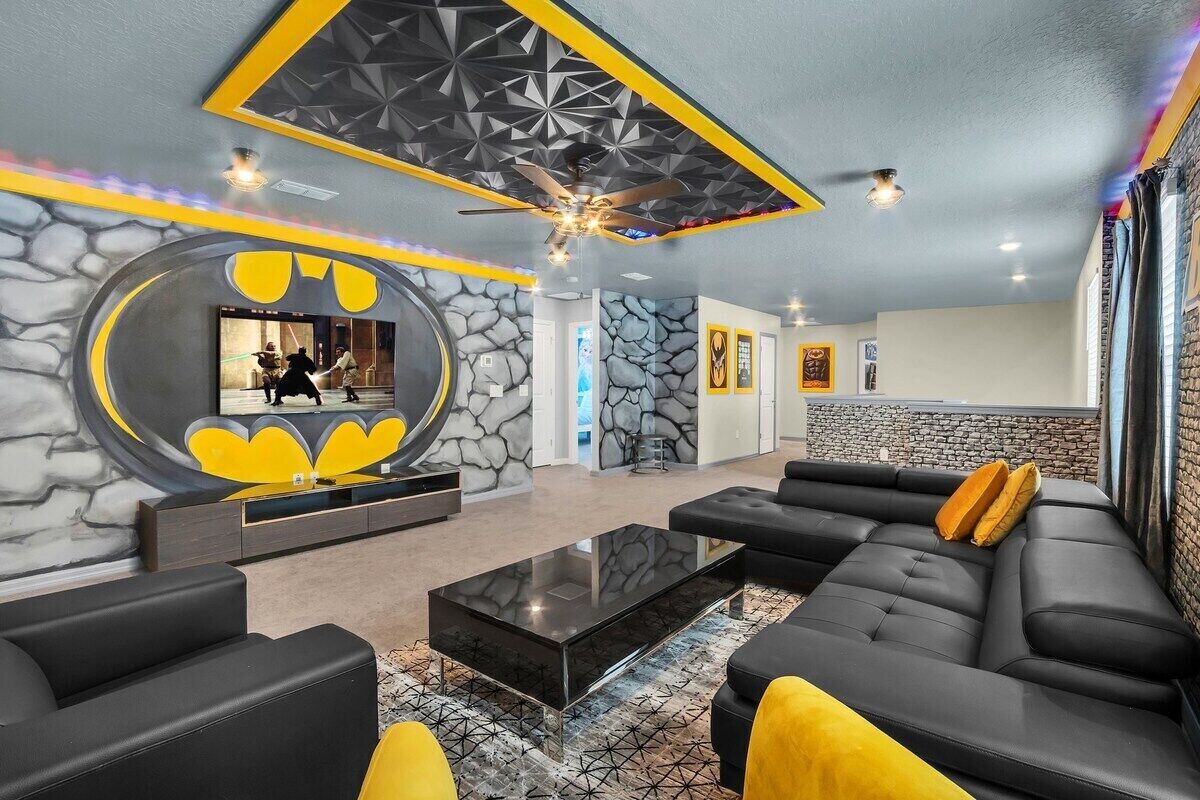 A modern living room with a stone wall, black leather sofas, a glass coffee table, and a ceiling fan.