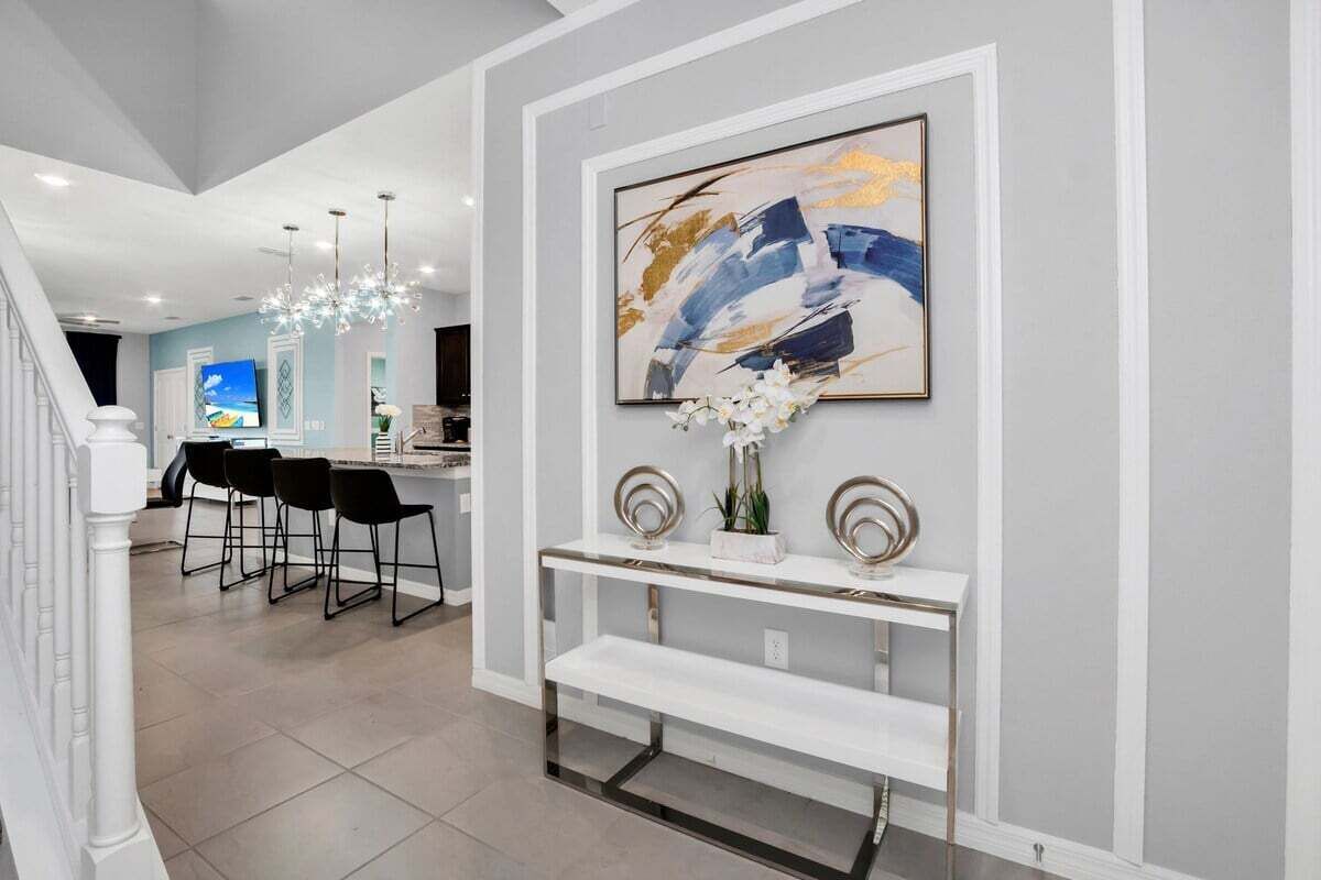 Un salón moderno con una consola blanca, un cuadro abstracto grande y una escalera que lleva a otra habitación.