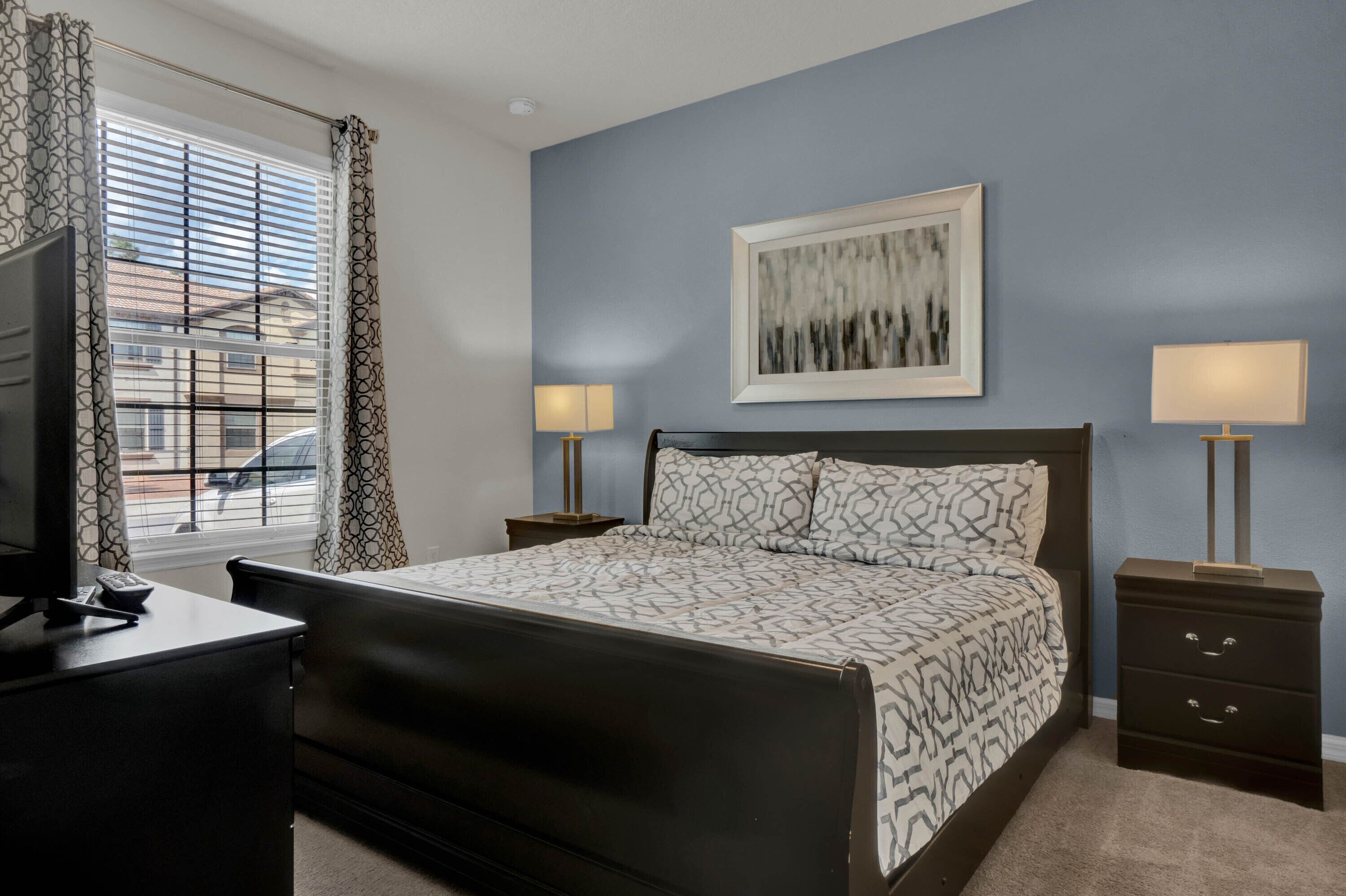 A bedroom with a bed, bedside lamps, a desk, a TV, and a window with curtains.
