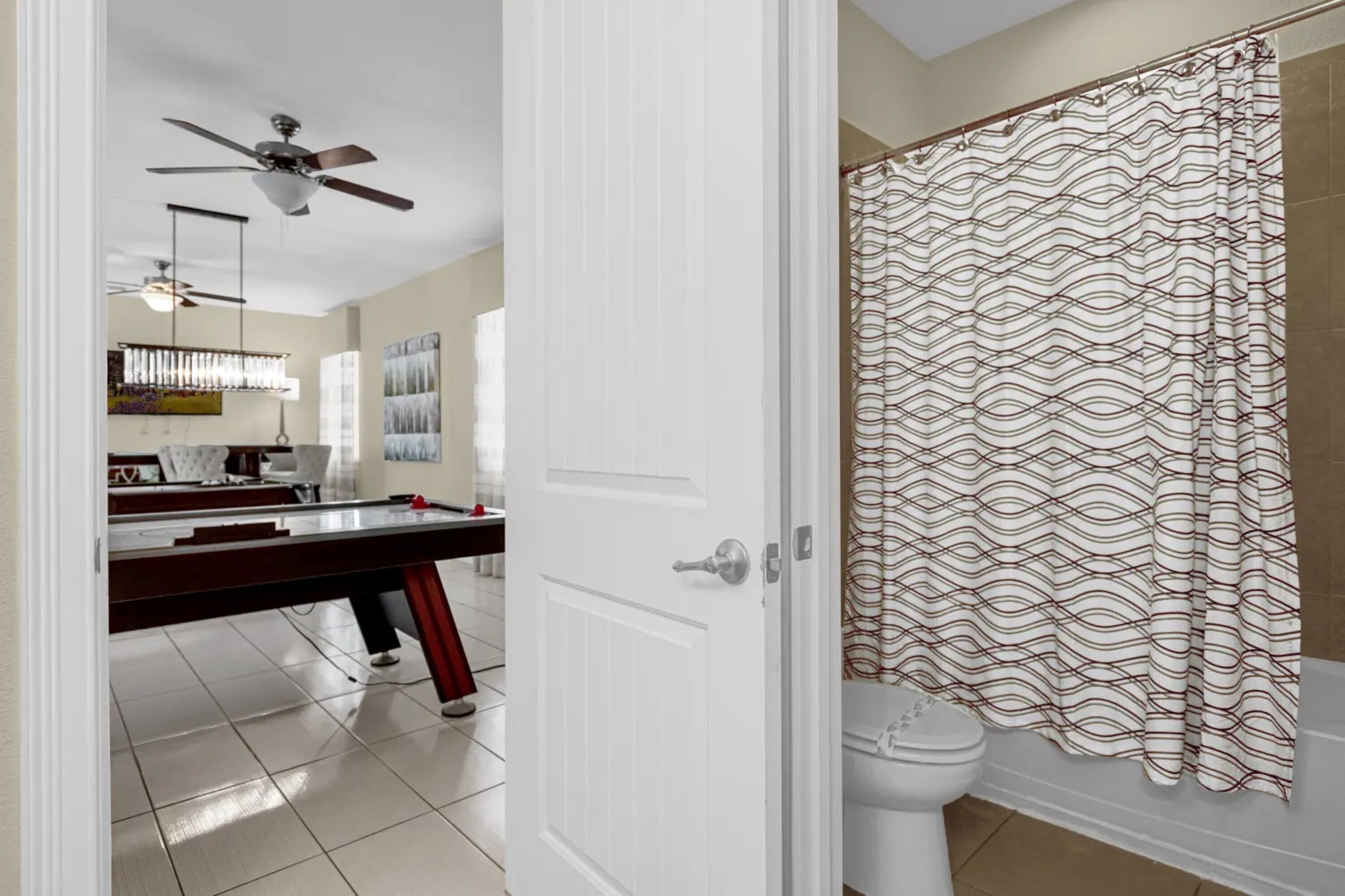 Un baño con cortina de ducha estampada, inodoro blanco y ventilador de techo.