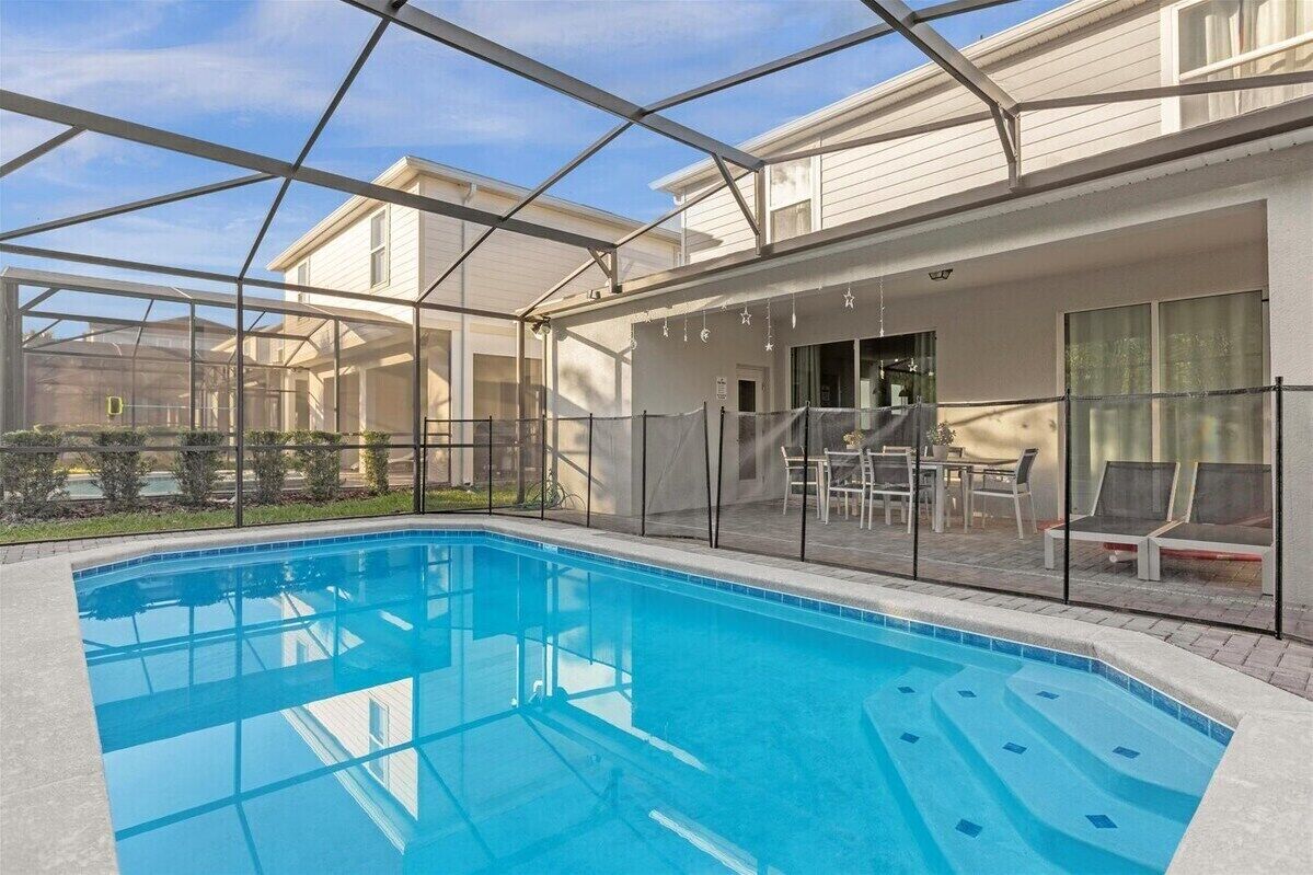 A swimming pool with a glass enclosure, surrounded by a patio area with outdoor furniture.
