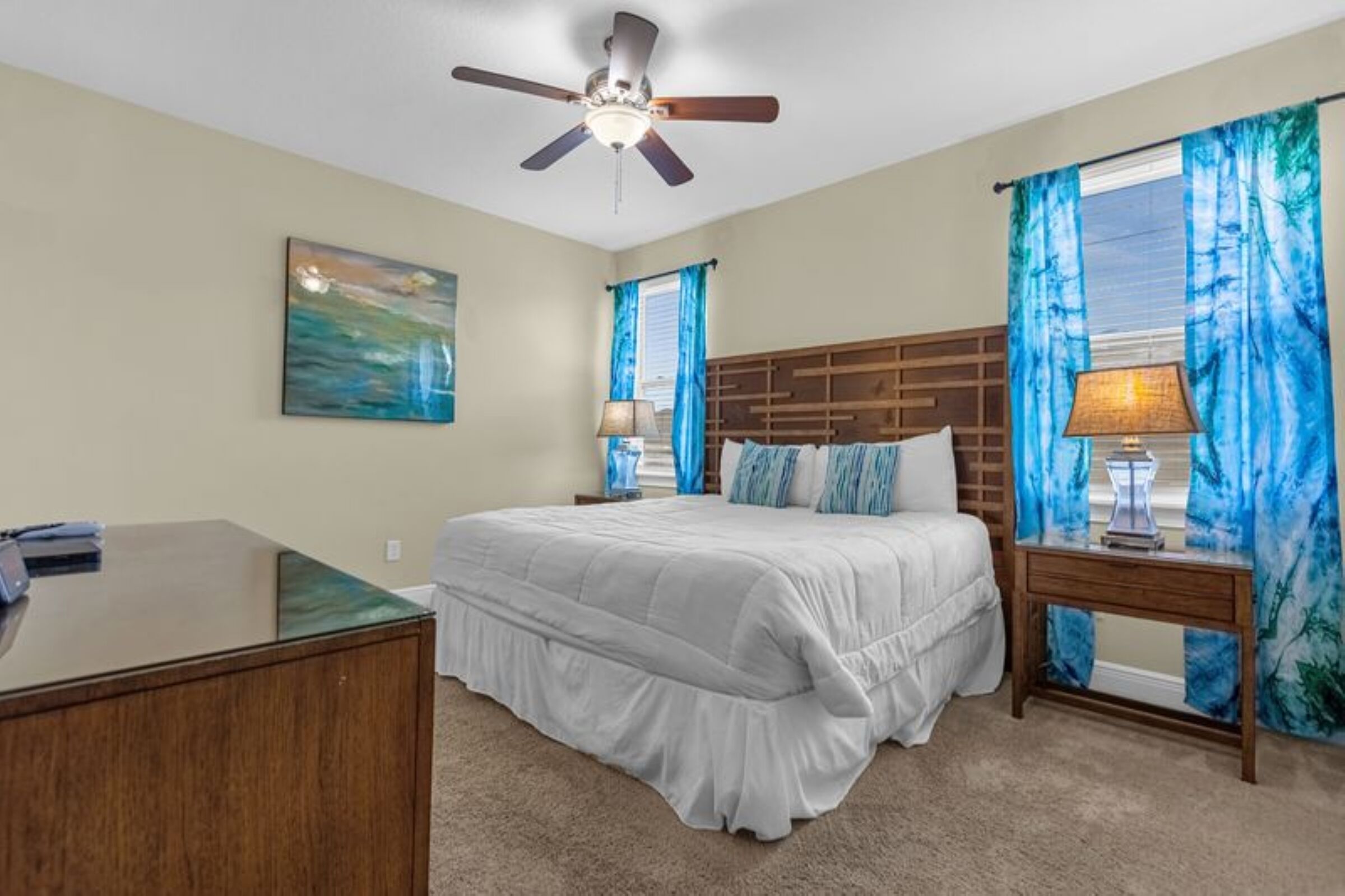 A bedroom with a bed, a desk, a ceiling fan, and a window with curtains.