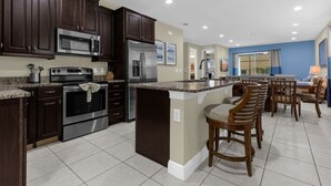 A modern kitchen with dark wood cabinets, stainless steel appliances, and a central island with bar stools. - 431-7-np-gateaway With Screened Pool (Kissimmee)