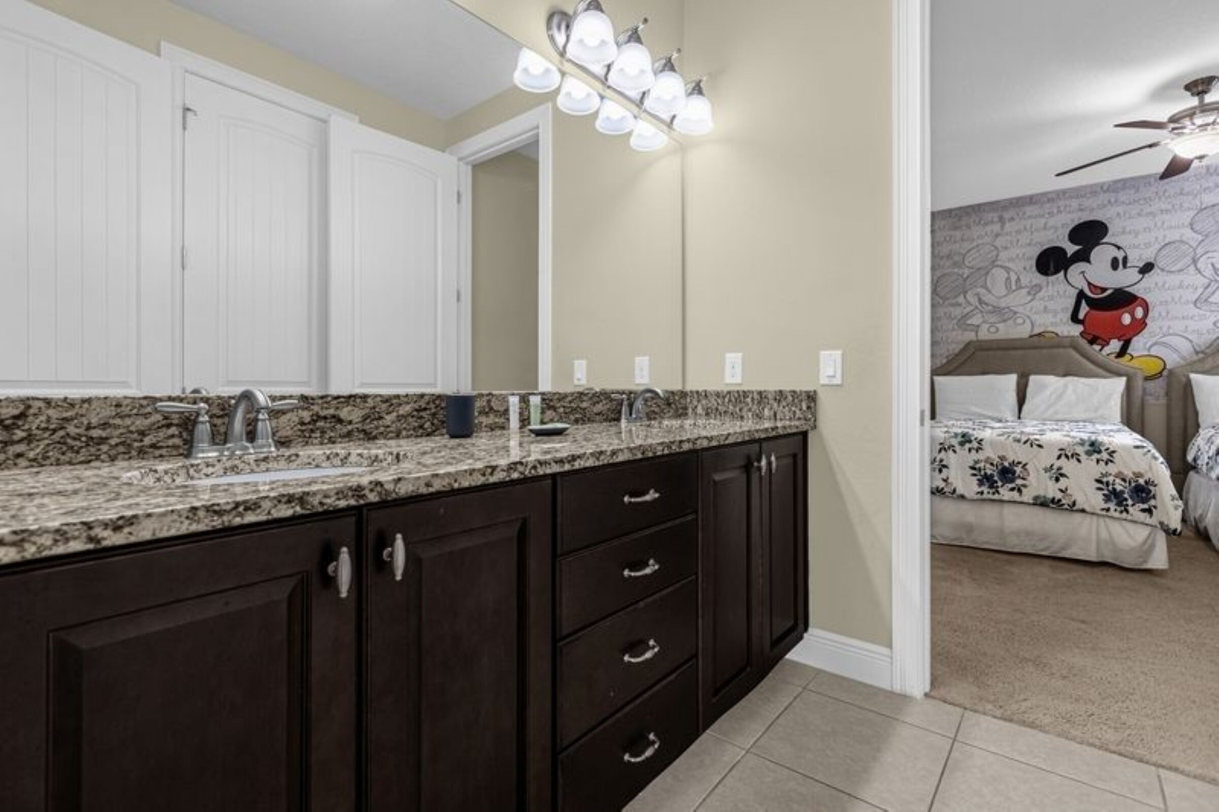 A bathroom with dark cabinets, a granite countertop, and a Mickey Mouse mural on the wall.