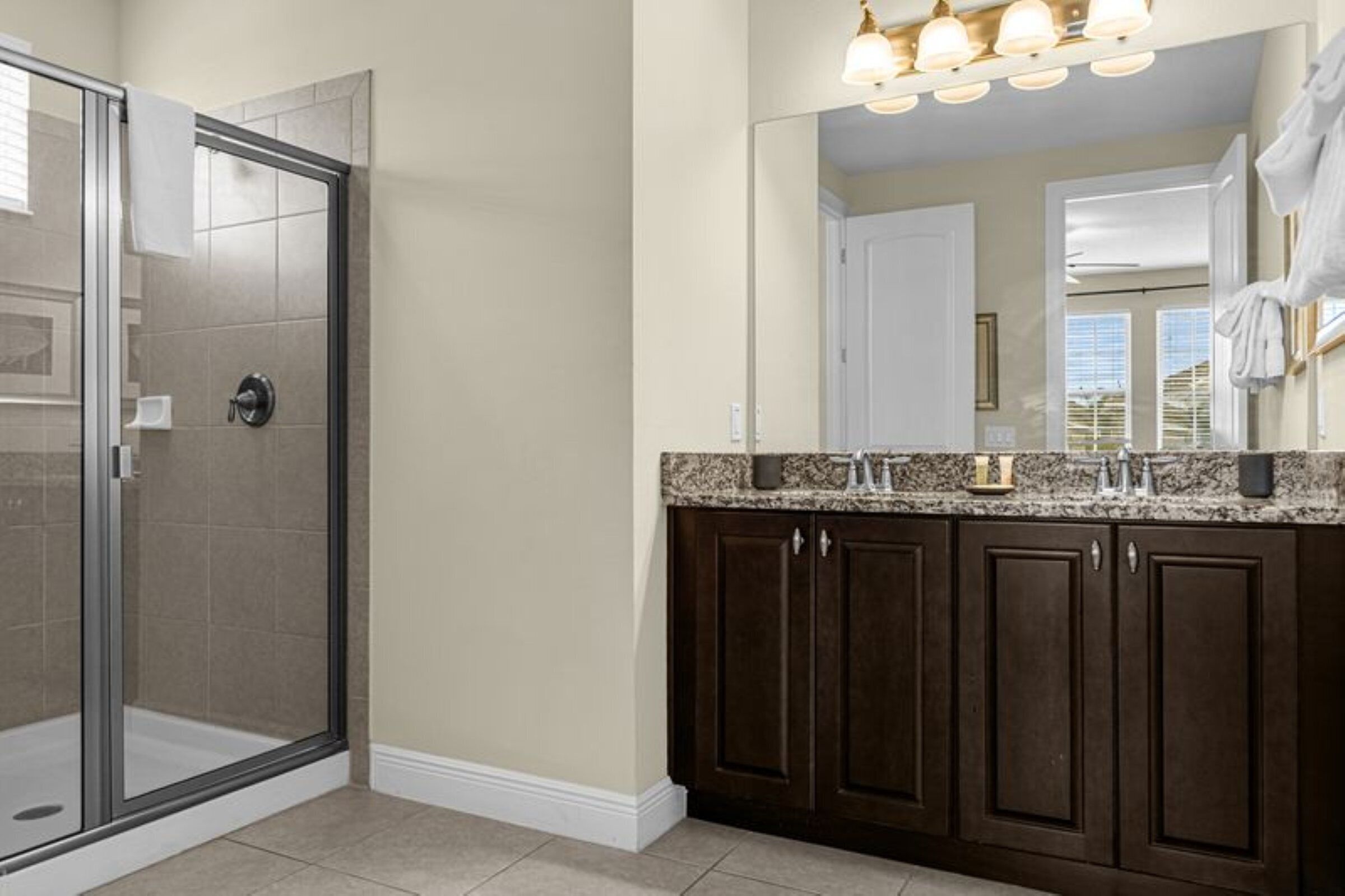 A bathroom with a shower, a vanity with dark cabinets, and a large mirror.