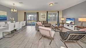 Ein modernes Wohnzimmer mit Essbereich, einer Couch, einem Fernseher und Blick auf einen Pool.