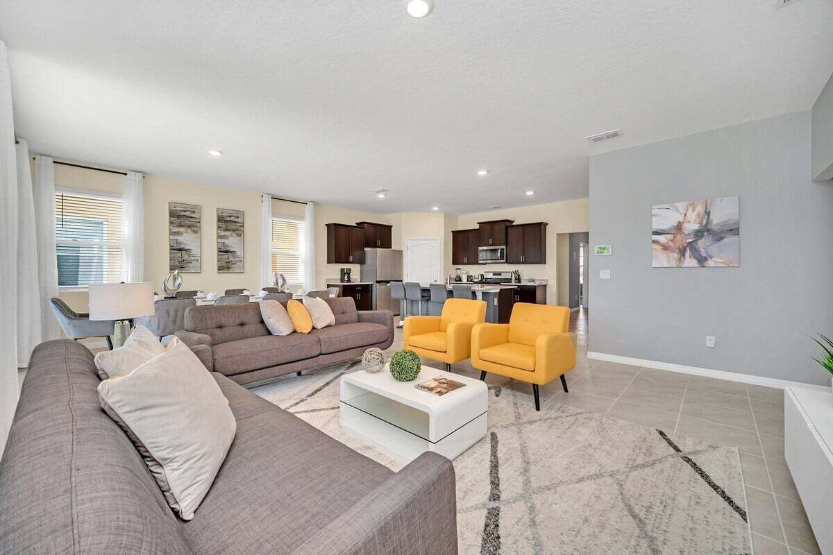 A modern living room with a sofa, armchairs, a coffee table, and a kitchen in the background.