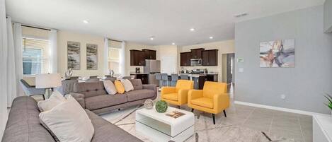 A modern living room with a sofa, armchairs, a coffee table, and a kitchen in the background.