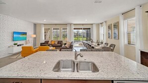 Een moderne keuken met een granieten aanrecht en een dubbele spoelbak, grenzend aan een eethoek met een tafel en stoelen.