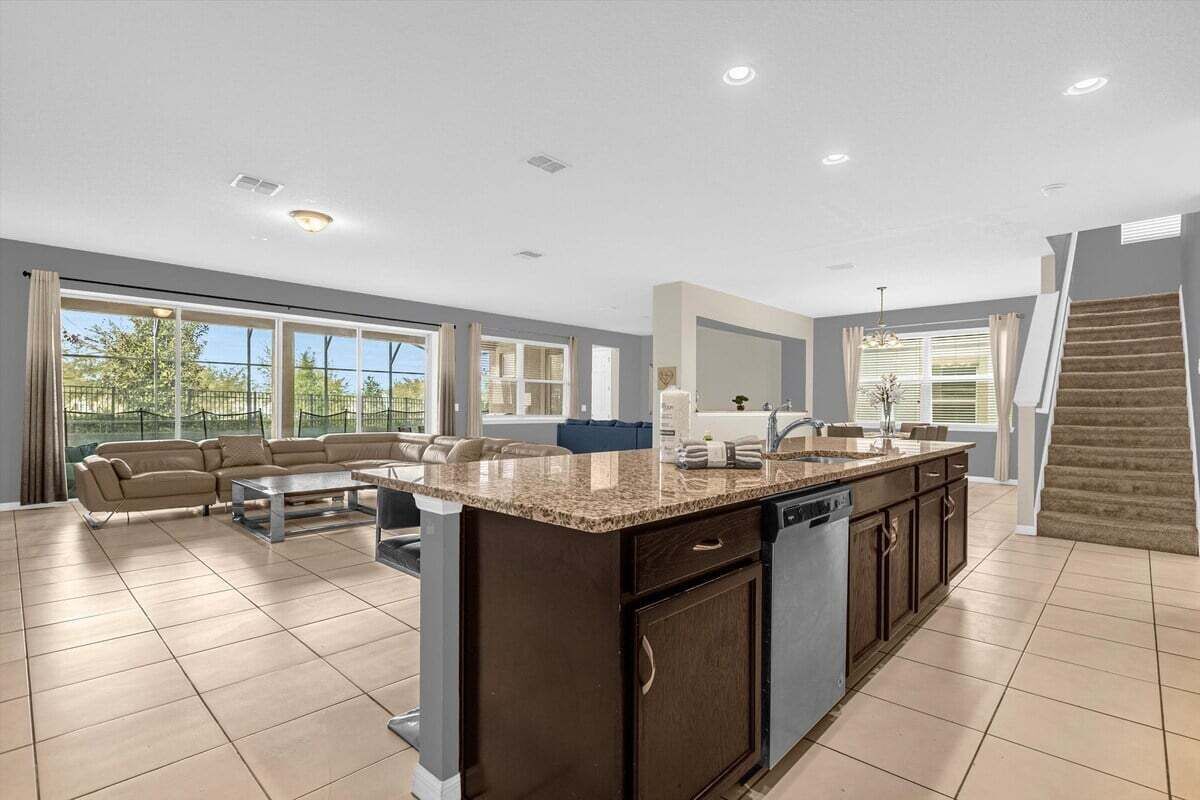 A spacious kitchen with a large island, a dining area with a sofa, and a view of the outdoors through large windows.