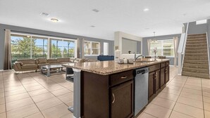 Une cuisine spacieuse avec un grand îlot central, un coin repas avec un canapé et une vue sur l’extérieur grâce à de grandes fenêtres.