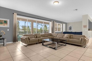 A spacious living room with a sectional sofa, a coffee table, and large windows offering a view of the outdoors. - 9031srl Luxury 9beds Villas With Pool Spa In Solara (Kissimmee)