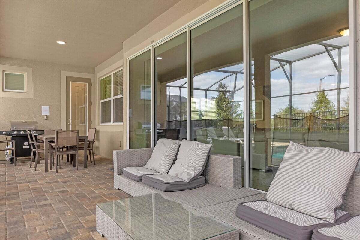 An outdoor living area with a sofa, chairs, a glass table, and a barbecue grill.