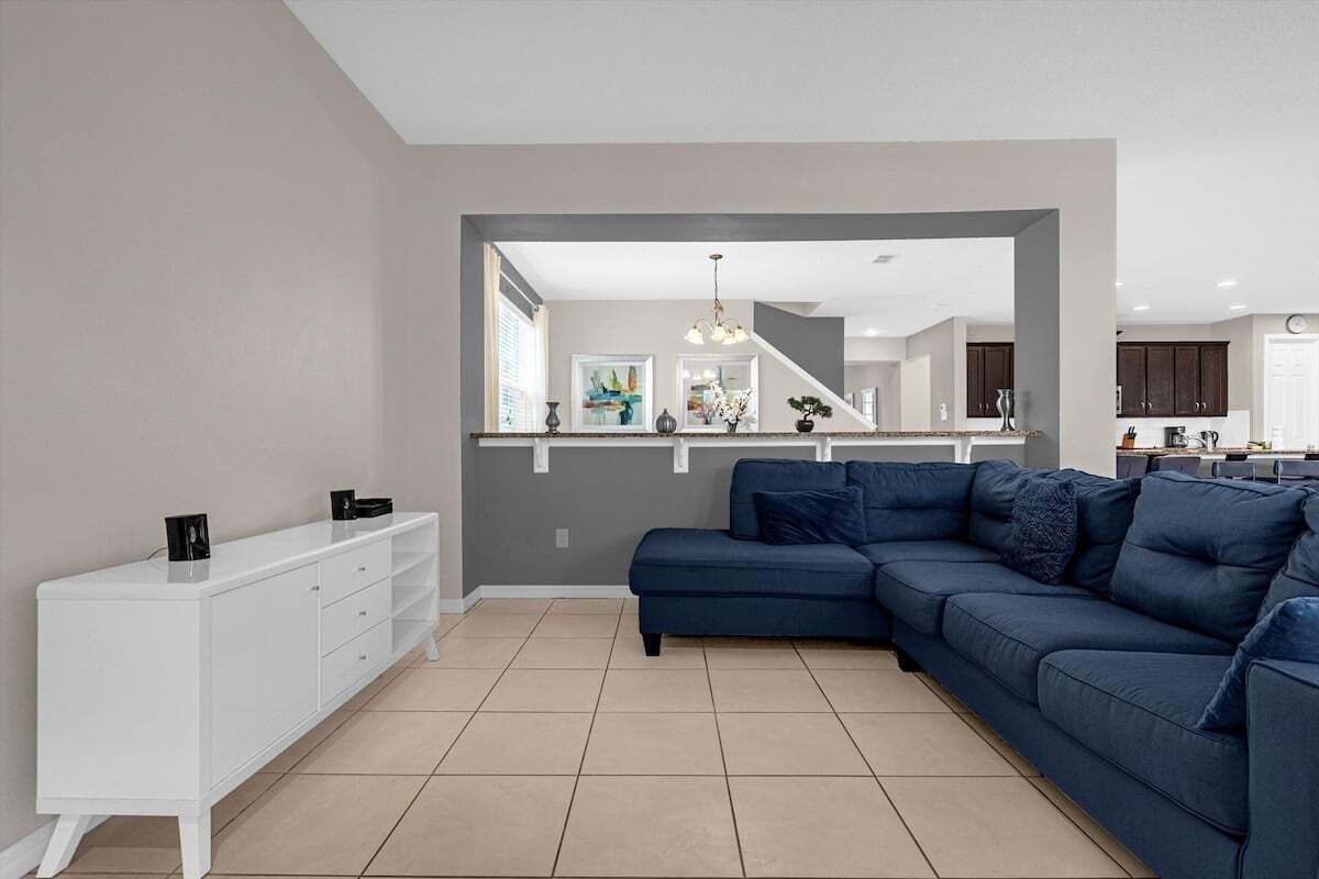 A modern living room with a dark blue sofa, a white console table, and a kitchen in the background.