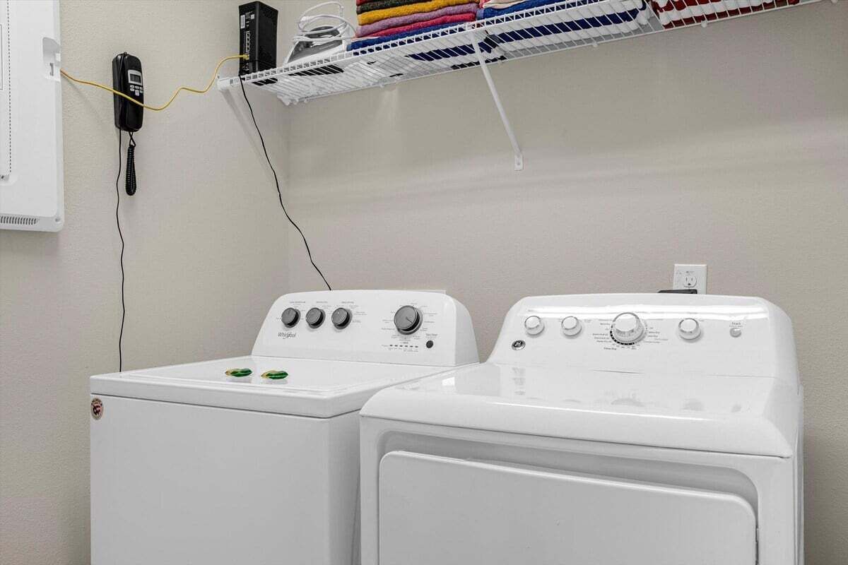 A laundry area with two white washing machines, a wall-mounted phone, and a shelf with folded towels.