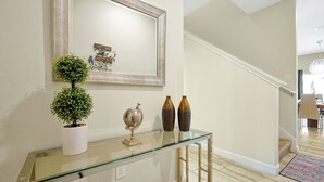A glass console table with decorative items, a framed mirror, and a staircase leading to another room. - 1576 Moon,champions Gate,4bed (Davenport)