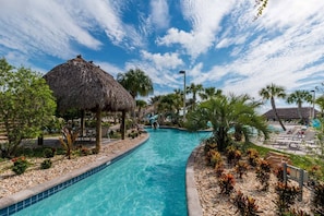 A swimming pool with a thatched-roof structure, palm trees, and lounge chairs. - 1576 Moon,champions Gate,4bed (Davenport)