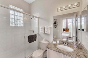 A modern bathroom with a glass shower enclosure, a white toilet, a granite countertop sink, and a large mirror. - 904 Lockbreeze Drive Davenport, 4bed (Davenport)