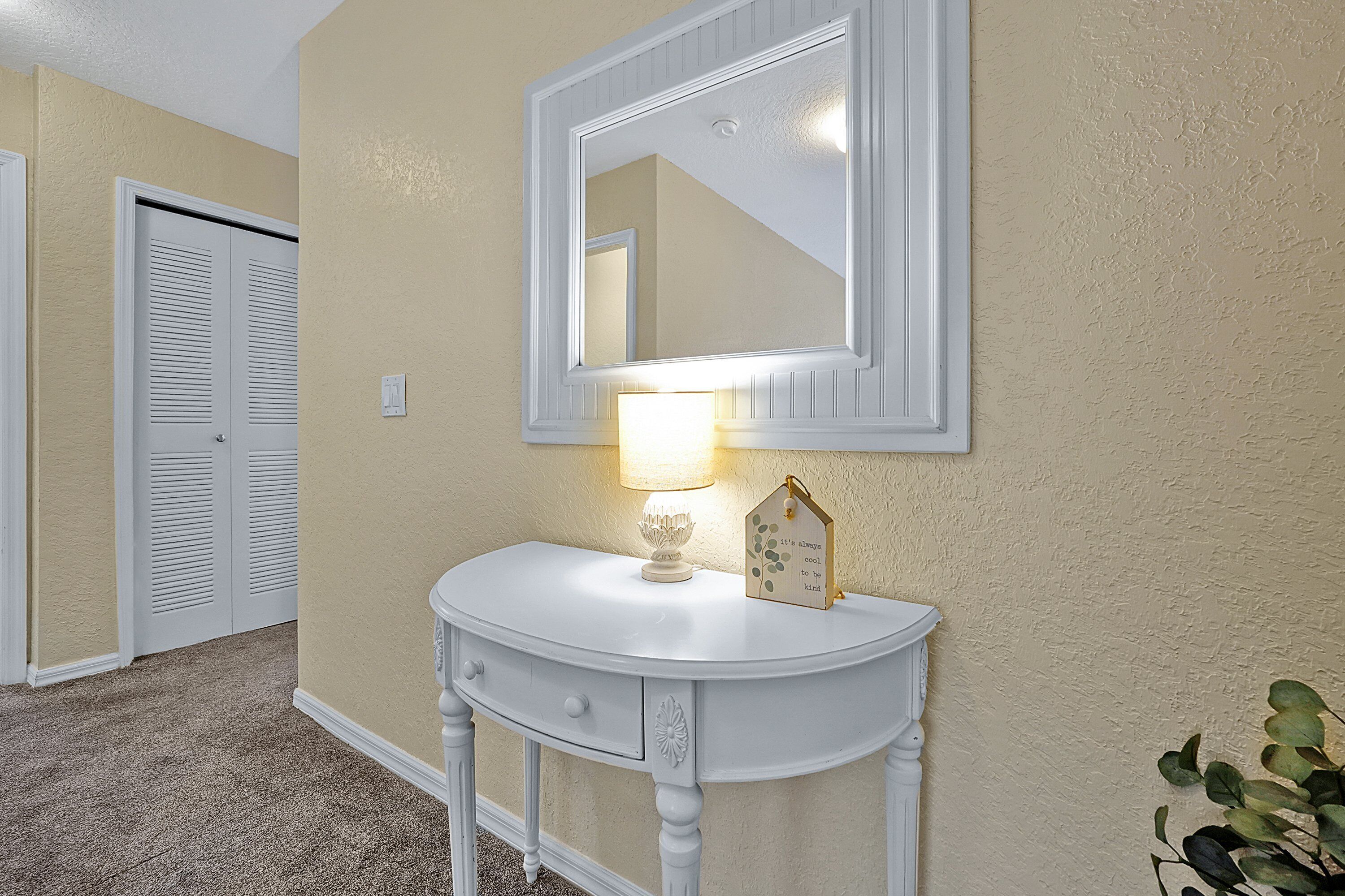 Une coiffeuse blanche avec un miroir, une lampe et un objet décoratif en forme de maison.