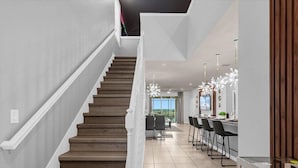 A modern kitchen with a central island, a dining area with chairs, and a staircase with wooden steps. - 1891sd · Brand New 7br/pool/spa/ Disney Fireworks View (Davenport)